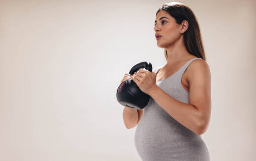 Eine schwangere Frau trainiert in einem Studio, hebt Gewichte und konzentriert sich während ihres dritten Trimesters auf ihr Wohlbefinden. Sie legt Wert auf ihre Fitness und Selbstfürsorge während der Mutterschaft und demonstriert Krafttraining und Körperpflege. - JLPSF30878