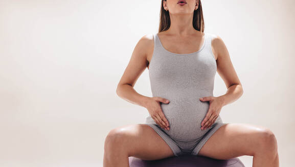Eine schwangere Frau im dritten Trimester übt in einem Studio pränatales Yoga. Mit einem Stabilitätsball zur Unterstützung konzentriert sie sich auf Flexibilität und Kraft. Mit Fitnessaktivitäten fördert sie ihr Wohlbefinden während der Schwangerschaft. - JLPSF30882