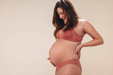 Pregnant woman in bra and panties holding stomach stock photo