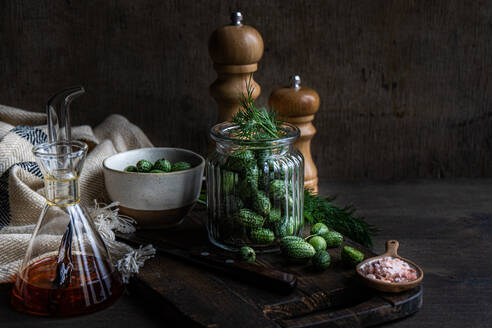 Ingredients for preparing cucamelon fermentation placed in jar placed on wooden tray near napkin and salt and pepper shakers against dark background - ADSF48520