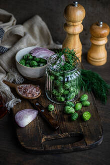 High angle of ingredients for preparing cucamelon fermentation placed in jar placed on wooden tray near napkin and salt and pepper shakers against dark background - ADSF48521