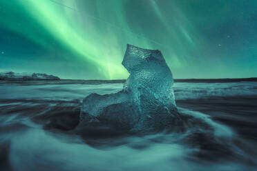 Picturesque scenery of rippling sea water with pieces of broken ice in black sandy beach against Aurora Borealis green sky in Diamond Beach in Iceland - ADSF48640