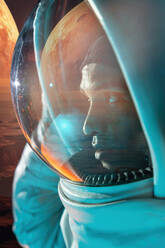 Side view of male ethnic astronaut in spacesuit looking through glass at reflective red planet in space - ADSF48694