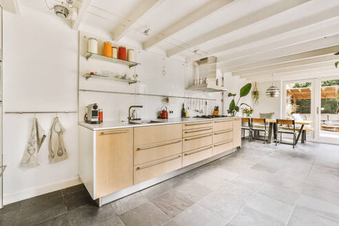 Interior of spacious kitchen with large countertop and cabinets by dining area at contemporary house - ADSF48727