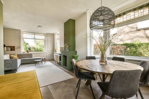 Dining table with chairs arranged by windows in spacious living room with sofa and fireplace in contemporary apartment - ADSF48735