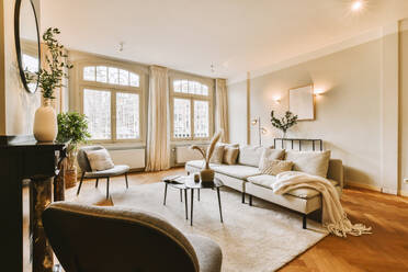 Comfortable couch and coffee table arranged in front of fireplace in light spacious living room with large windows - ADSF48737