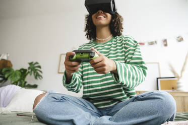 Glückliches Mädchen trägt Virtual-Reality-Simulatoren und spielt ein Videospiel mit Controller im Schlafzimmer - ALKF00665