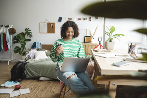 Smiling girl using laptop near desk at home - ALKF00677