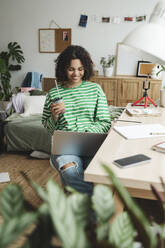 Happy teenage girl using laptop near desk at home - ALKF00682