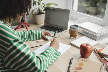 Curly haired girl making notes on note pad at desk - ALKF00684