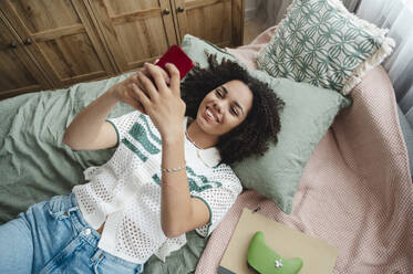 Glückliches Mädchen auf dem Bett liegend und mit Smartphone zu Hause - ALKF00709