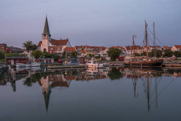 Dänemark, Bornholm, Ronne, St.-Nikolaus-Kirche und umliegende Häuser spiegeln sich in der Abenddämmerung im Küstenwasser - KEBF02764