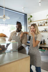 Happy barista with colleague standing and laughing at coffee shop - EBSF03971