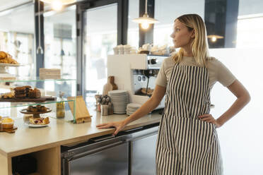 Nachdenklicher Barista mit Hand auf der Hüfte in der Nähe des Tresens eines Cafés - EBSF03980