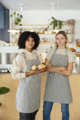 Happy barista holding cupcakes with colleague in coffee shop - EBSF03989