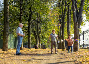 Junge macht Seifenblasen mit Großeltern im Park an einem sonnigen Tag - MBLF00052