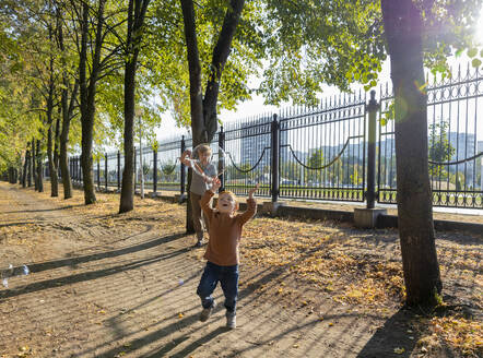 Junge jagt Seifenblasen mit Großmutter im Hintergrund im Herbst Park - MBLF00053