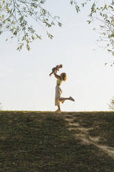 Playful mother holding baby boy in park - NDEF01280