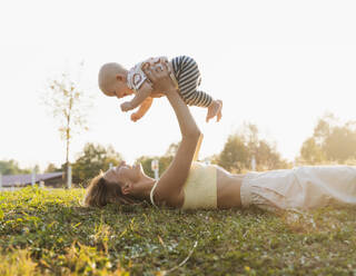 Mother lying on grass and playing with baby boy at park - NDEF01282