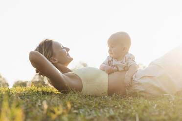 Glückliche Mutter liegt mit ihrem Sohn im Park bei Sonnenuntergang im Gras - NDEF01284