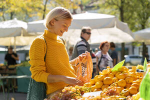 Lächelnde Frau kauft Mandarinen auf dem Bauernmarkt - NDEF01301