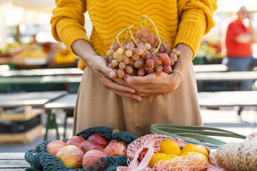 Woman holding bunch of grapes with apples and tangerines at farmer's market - NDEF01303