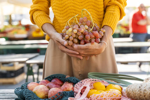 Frau hält Weintrauben mit Äpfeln und Mandarinen auf dem Bauernmarkt - NDEF01303