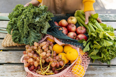 Mesh bags with fresh fruits and vegetables on table at farmer's market - NDEF01309