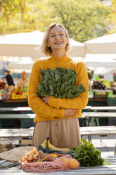 Smiling woman holding fresh kale at farmer's market - NDEF01312