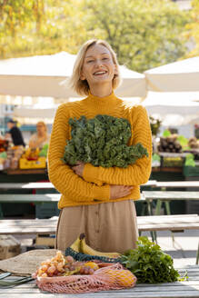 Lächelnde Frau mit frischem Grünkohl auf dem Bauernmarkt - NDEF01312