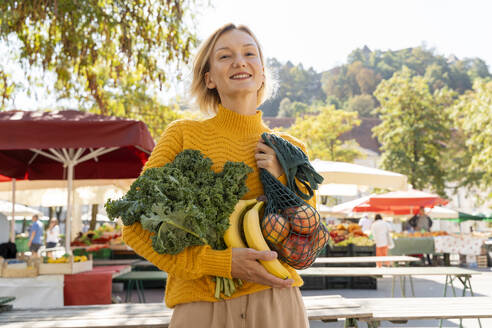 Smiling woman holding fresh and vegetables at farmer's market - NDEF01314