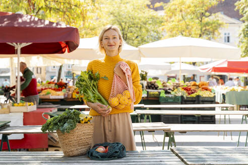 Lächelnde Frau mit Tüten voller Obst und Gemüse auf dem Bauernmarkt - NDEF01315