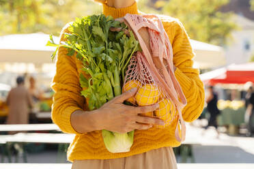 Woman holding celery and mesh bag with tangerines at farmer's market - NDEF01316