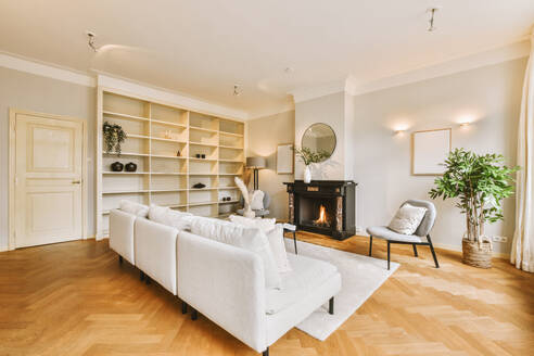 Interior of living room with comfortable sofa and chairs with fireplace in light white house with large shelves - ADSF48754