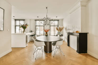 Interior of stylish dining room with chandelier hanging over table and chairs by fireplace in modern apartment - ADSF48755