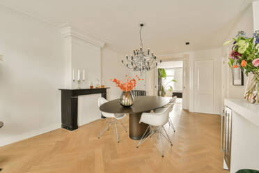 Interior of dining room with chandelier hanging over table and chairs by fireplace in apartment surrounded with white walls - ADSF48756