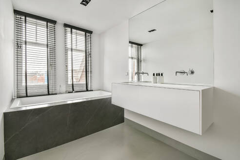 Interior of white bathroom with large bathtub and sink with clean mirror in modern apartment with white walls - ADSF48757