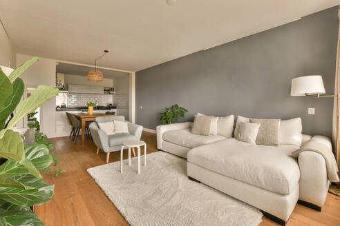 Interior of living room with white comfortable couch by dining area in front of gray wall in modern apartment - ADSF48759