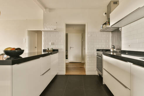 Interior of spacious kitchen with white cabinets and black countertops with tiled wall in modern apartment - ADSF48763