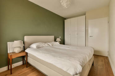 Interior of modern comfortable bedroom with white bed by night table and wardrobe in front of green wall - ADSF48764