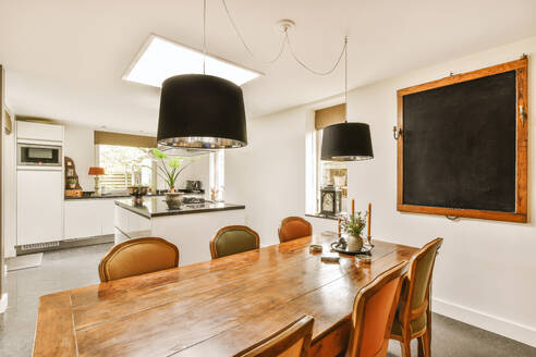 Pendant lights hanging over wooden dining table and chairs placed in front of open plan kitchen at home - ADSF48770