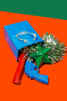 Hoher Winkel von blauen Karton Tasche auf roter Oberfläche mit Lametta, bunten Spielzeugpistolen und grünen Stern vor grünem Hintergrund platziert - ADSF48786