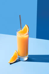 Squeezed orange juice garnished with orange slice on blue background - ADSF48795
