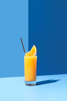 Squeezed orange juice garnished with orange slice on blue background - ADSF48796