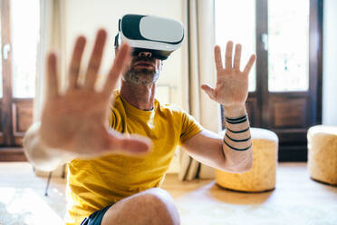 Bearded male in VR goggles outstretching arms while training in light apartment - ADSF48804