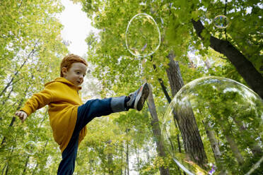 Verspielter Junge, der im Herbstwald Seifenblasen wirft - MBLF00062