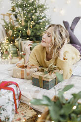 Happy woman lying on bed near Christmas presents in bedroom - VBUF00456