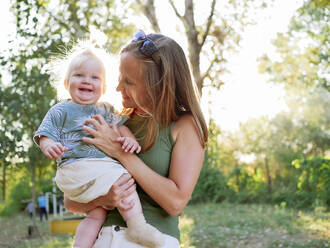 Happy mother carrying cute baby girl in park on sunny day - NLAF00156