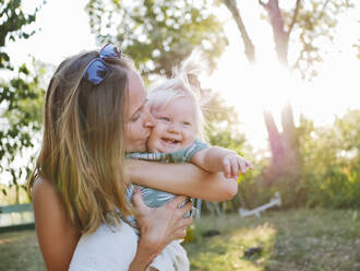 Mother kissing smiling daughter at park - NLAF00158