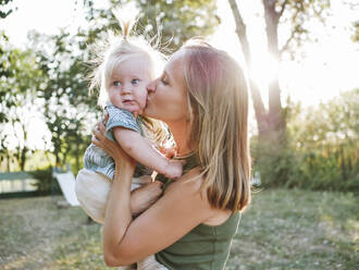 Woman kissing cute daughter in ponytail at park - NLAF00160